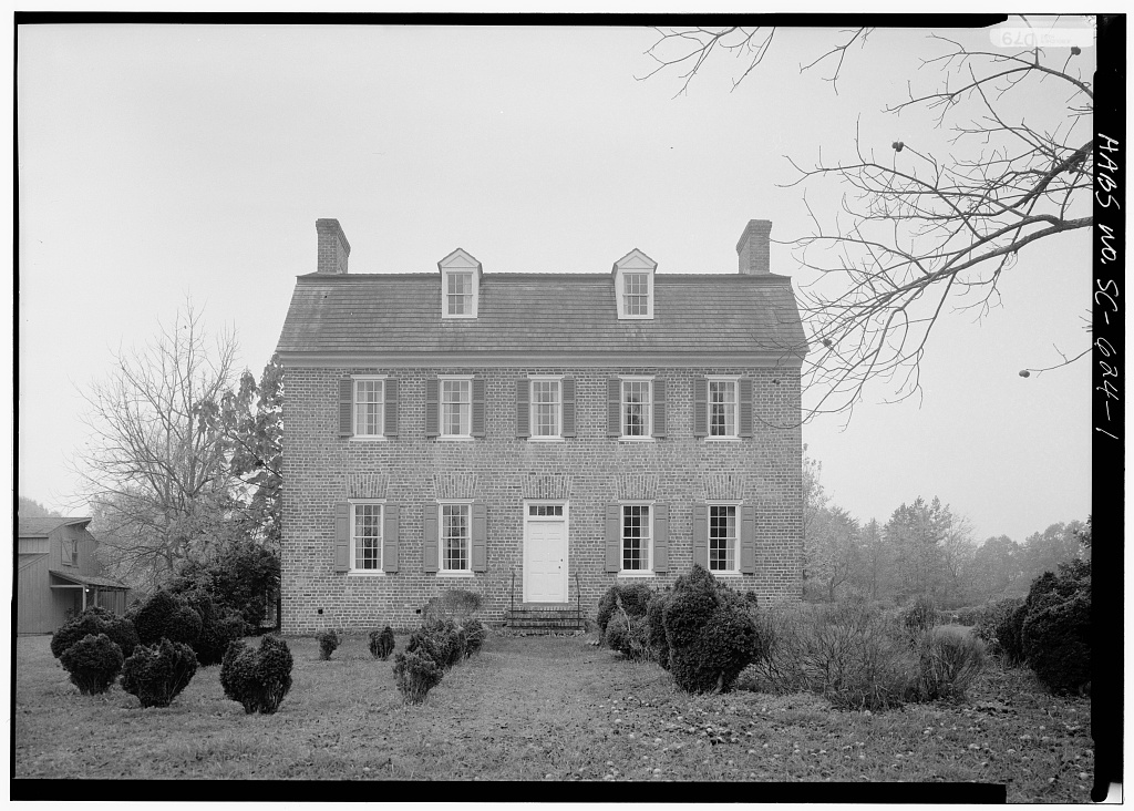 Black-and-white photograph of the Price House: a two-and-a-half-story brick house with shuttered windows, a centered white door, two roof dormers and a chimney at each end, with a wooden outbuilding at left.