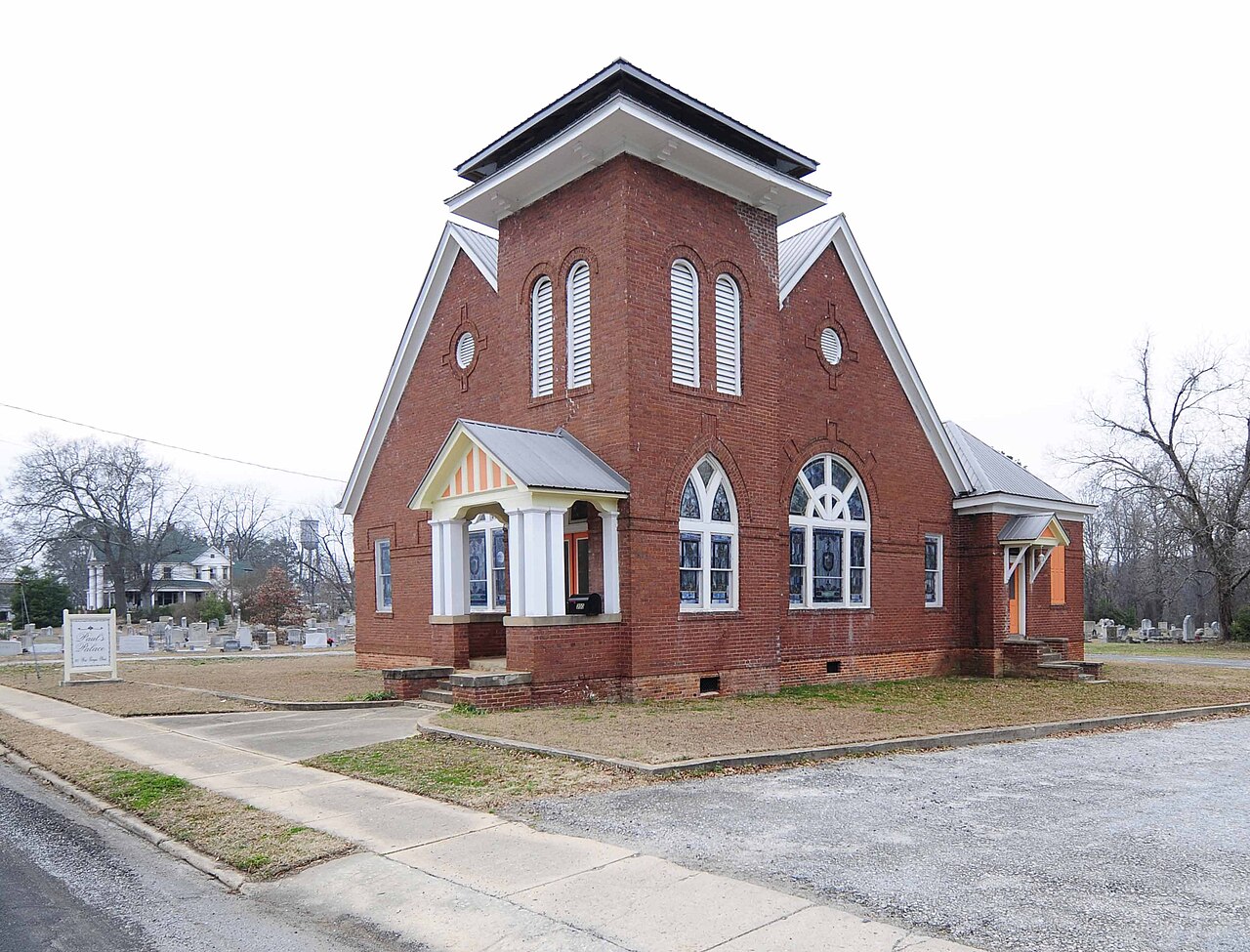 Color photograph of the 1911 red-brick First Presbyterian church building in Woodruff, with a square central tower, arched stained-glass windows, a white-columned entry porch and a metal roof, seen from the sidewalk.